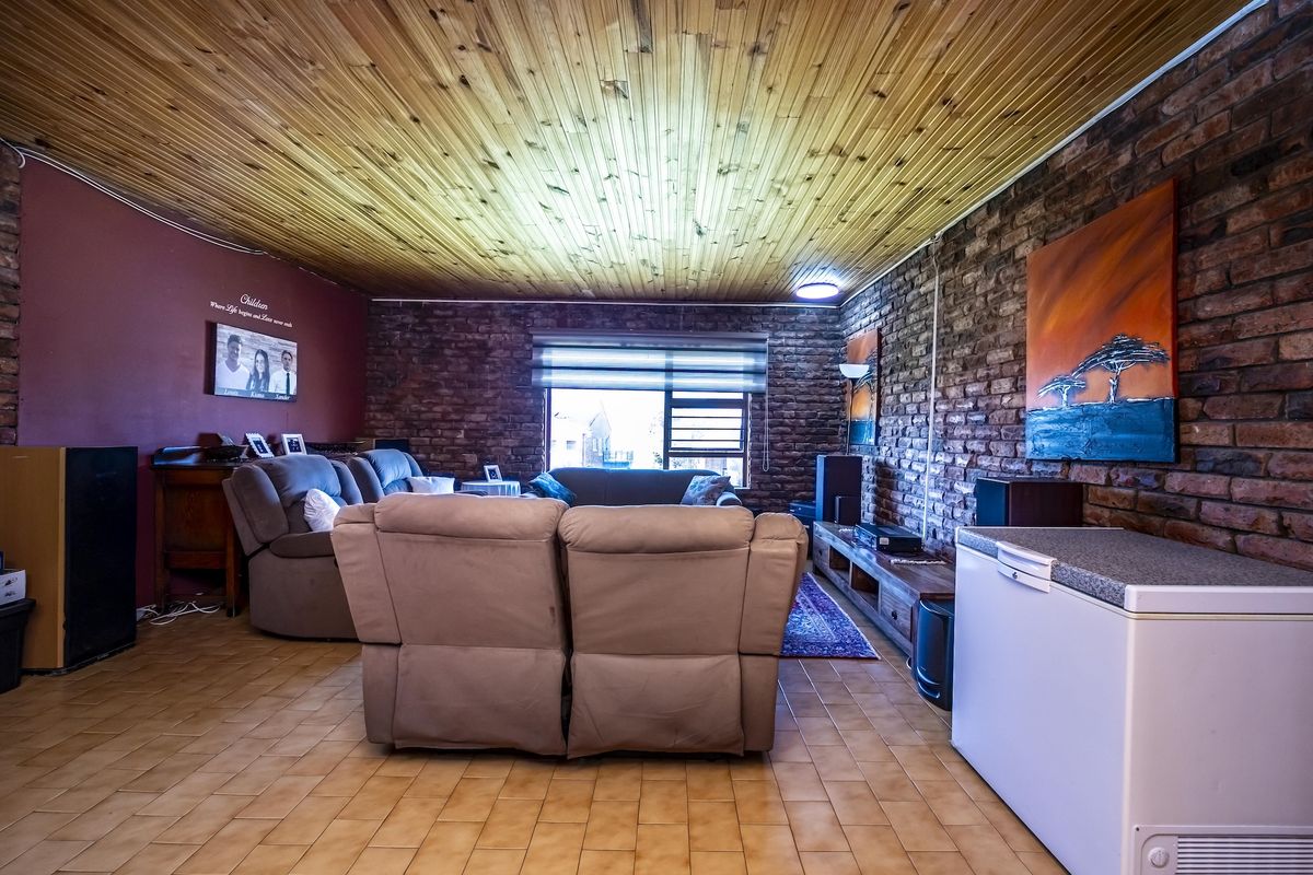 A living room featuring exposed brick walls, a timber-clad ceiling, and ceramic tile flooring, offering a rustic aesthetic with potential for modern updates.