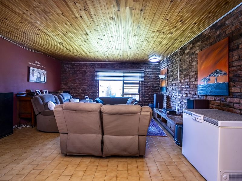 A living room featuring exposed brick walls, a timber-clad ceiling, and ceramic tile flooring, offering a rustic aesthetic with potential for modern updates.