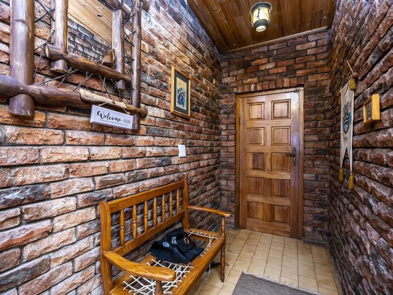 A rustic entrance hall featuring exposed brick walls, a timber panelled ceiling, and a solid wood door with ceramic tile flooring.