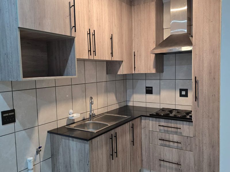 Modern compact kitchen featuring wood-look laminate cabinetry, black granite countertops, built-in hob, extractor fan, and neutral tiled finishes.