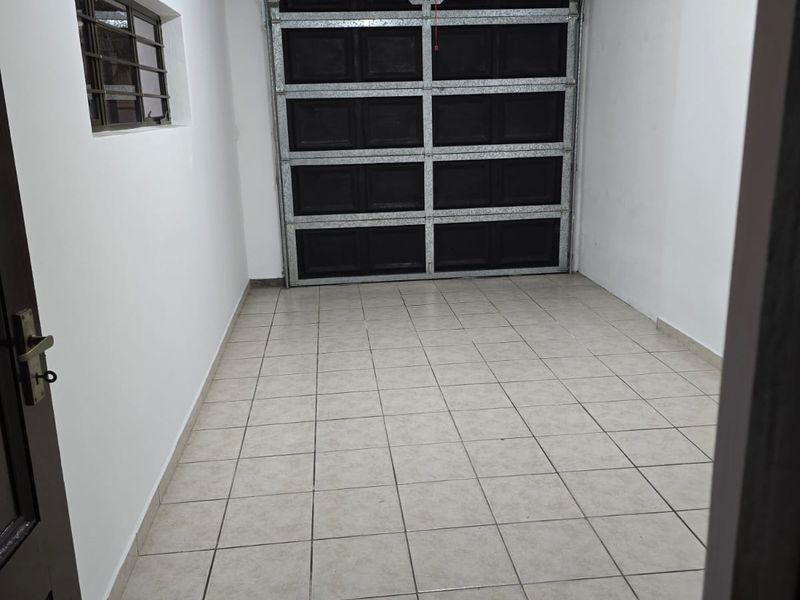 A clean, empty single-car garage featuring tiled flooring, a sectional garage door, and a side window with security bars.