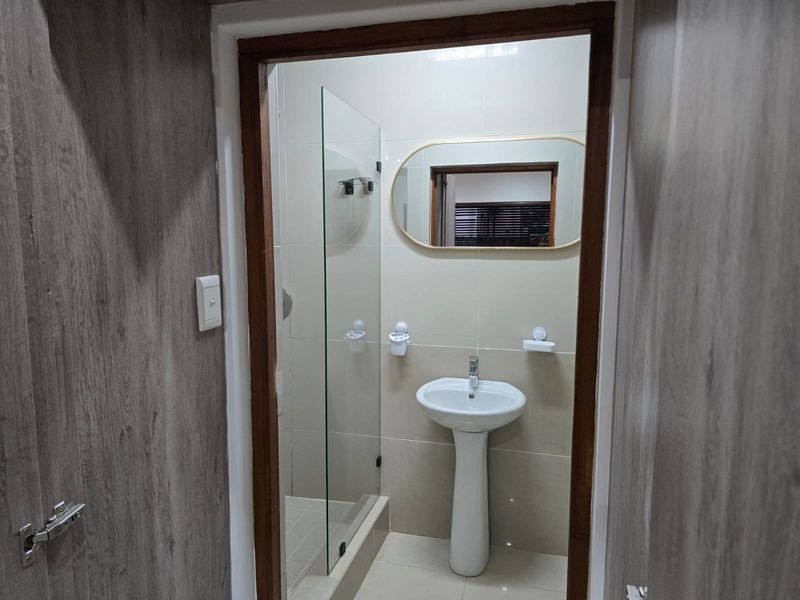 A clean, modern bathroom featuring a pedestal basin, tiled finishes, and a glass-enclosed shower area.