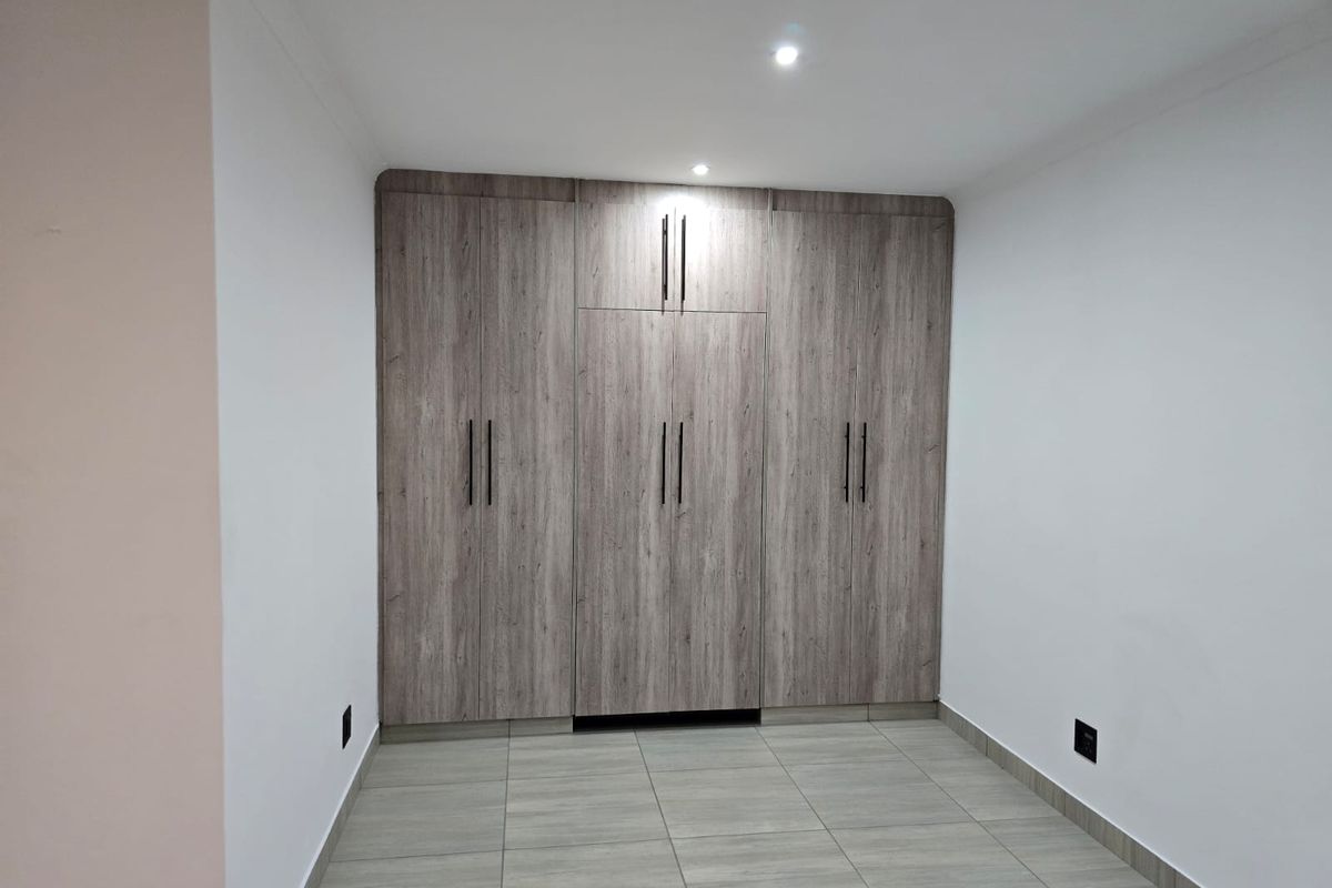 A clean, modern bedroom featuring neutral tiled flooring and extensive built-in wooden cupboards with contemporary black hardware.