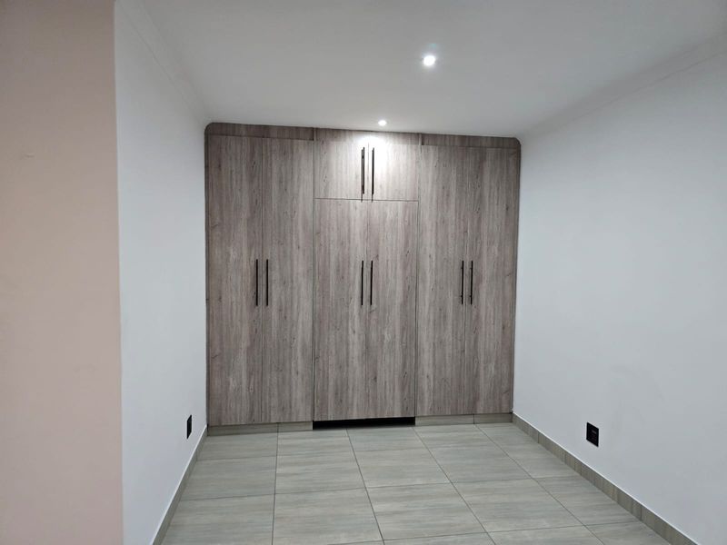A clean, modern bedroom featuring neutral tiled flooring and extensive built-in wooden cupboards with contemporary black hardware.