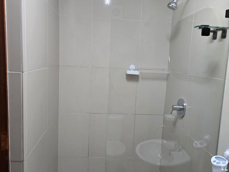 A clean, tiled shower enclosure featuring a glass screen, wall-mounted shower head, and mixer tap.