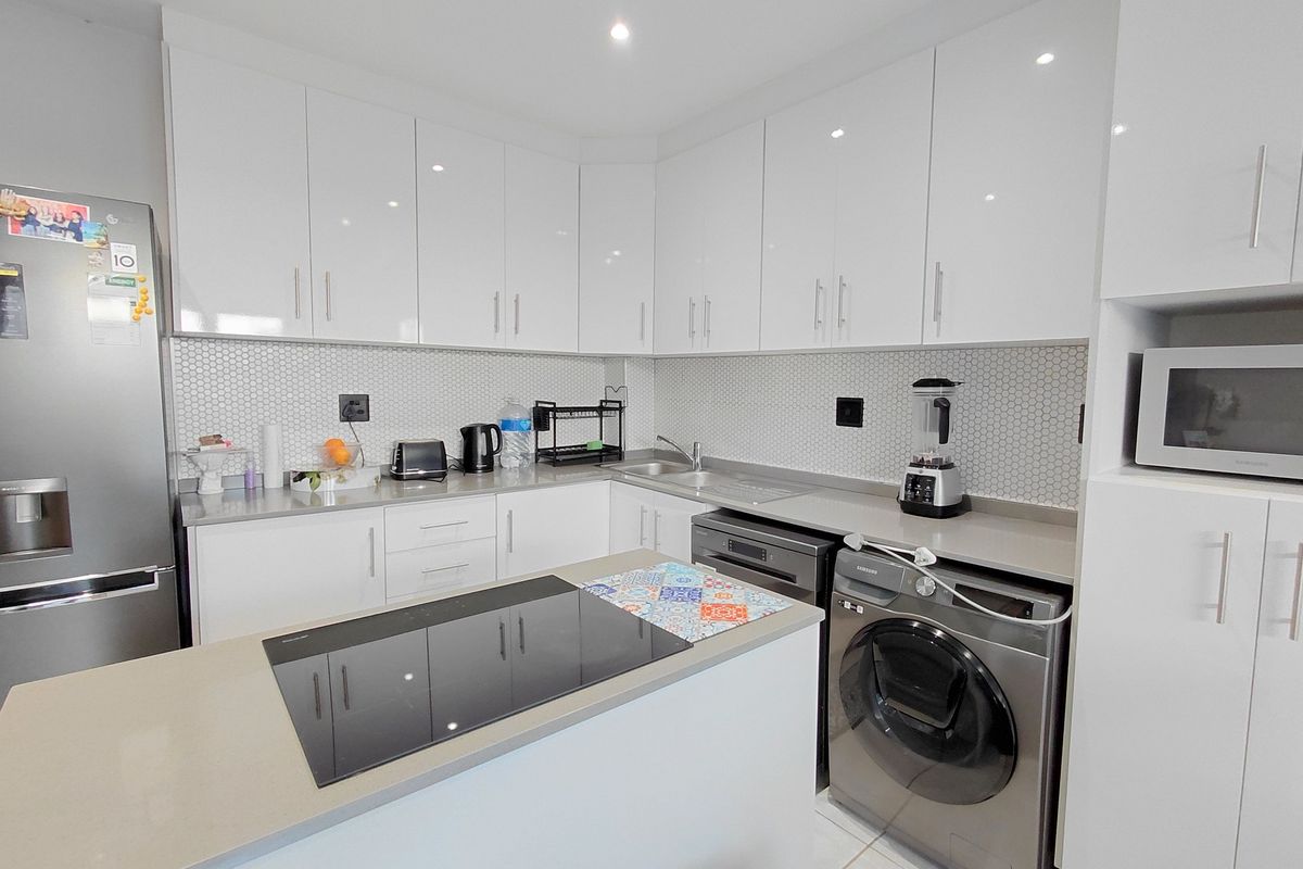 Modern kitchen featuring white high-gloss cabinetry, stone countertops, a mosaic tile backsplash, and integrated appliances including an induction hob and built-in microwave.