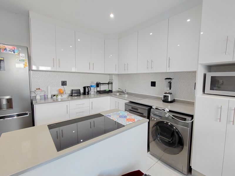 Modern kitchen featuring white high-gloss cabinetry, stone countertops, a mosaic tile backsplash, and integrated appliances including an induction hob and built-in microwave.