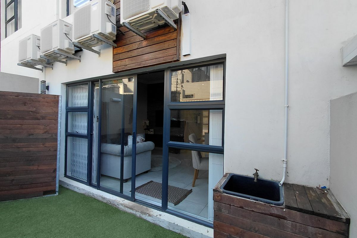 Rear exterior view of the apartment featuring sliding glass doors, wall-mounted air conditioning units, timber cladding accents, and a small utility sink area.