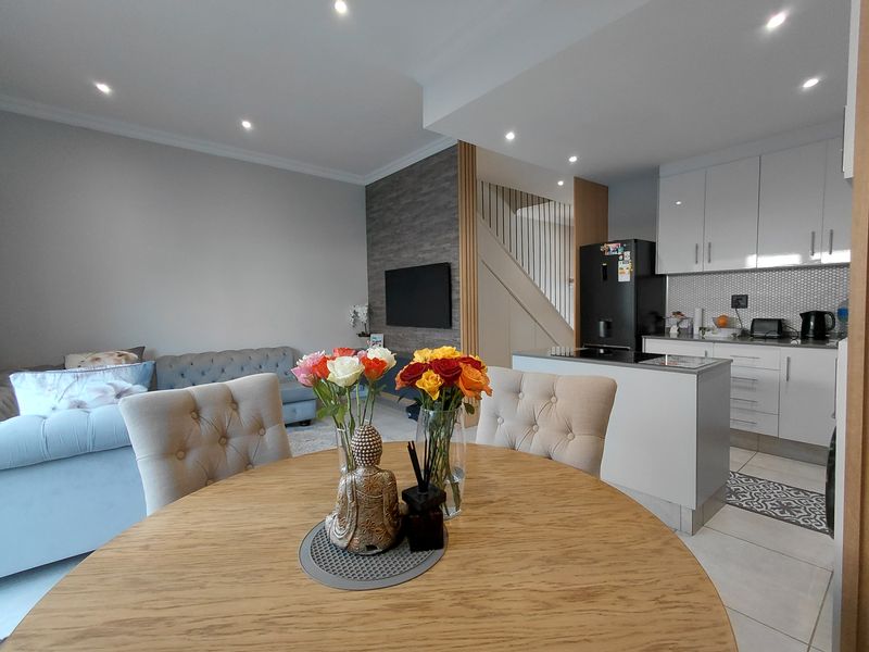 Modern open-plan living area featuring a contemporary kitchen with white cabinetry, stone countertops, and a feature wall, seamlessly flowing into the dining and lounge space.
