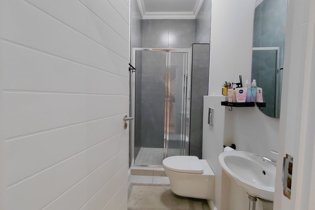 Modern bathroom featuring a wall-hung toilet, pedestal basin, and a glass-enclosed shower with contemporary grey wall tiling.