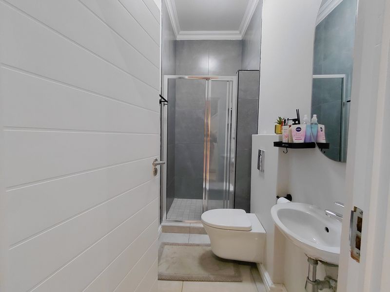 Modern bathroom featuring a wall-hung toilet, pedestal basin, and a glass-enclosed shower with contemporary grey wall tiling.
