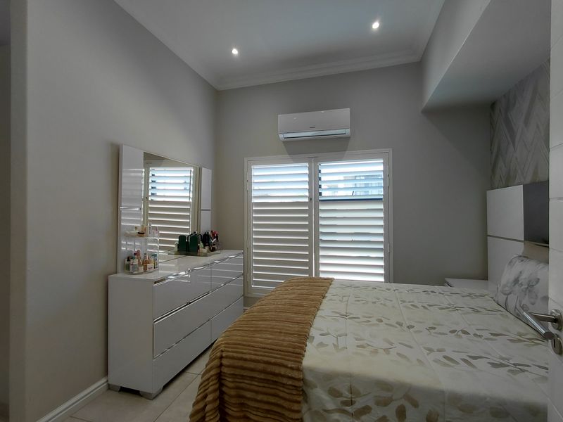 A well-maintained bedroom featuring tiled flooring, recessed downlights, an integrated air conditioning unit, and white plantation shutters for light control.