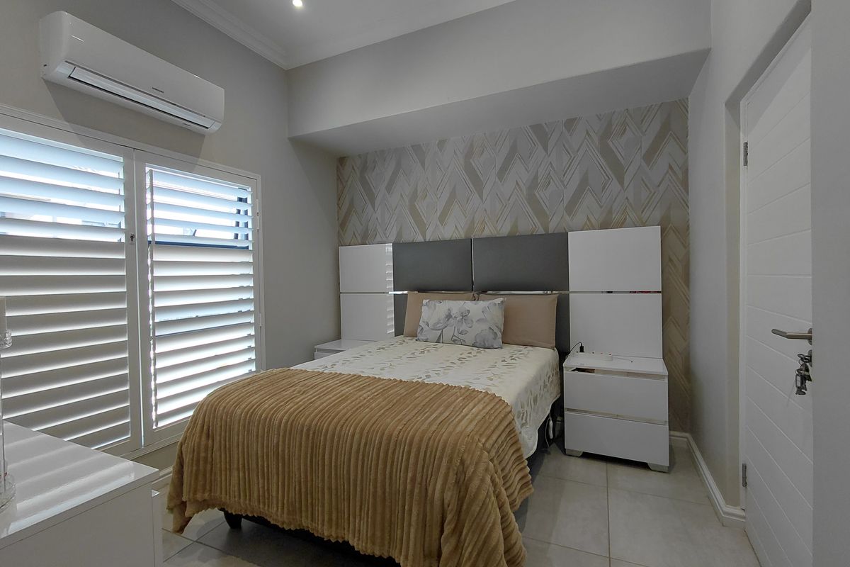 A well-maintained bedroom featuring tiled flooring, plantation shutters, a split-system air conditioner, and a modern built-in headboard with integrated storage.