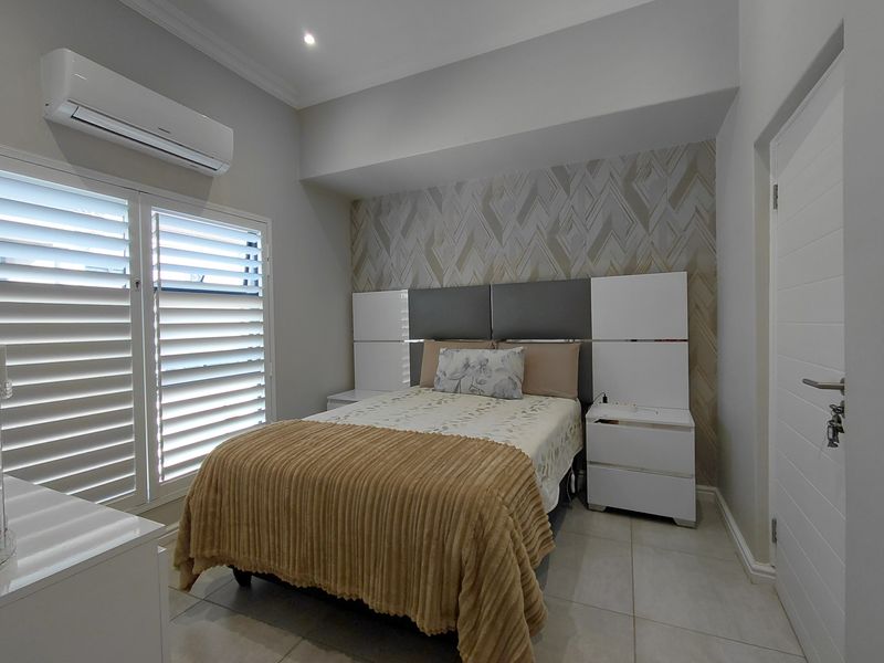 A well-maintained bedroom featuring tiled flooring, plantation shutters, a split-system air conditioner, and a modern built-in headboard with integrated storage.