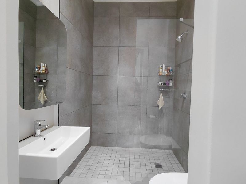 Modern bathroom featuring a walk-in shower with glass screen, large wall-mounted basin, and contemporary grey tiling throughout.