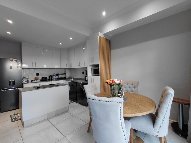 Modern open-plan kitchen featuring sleek white cabinetry, stone countertops, mosaic backsplash, and integrated appliances, seamlessly flowing into the dining area.