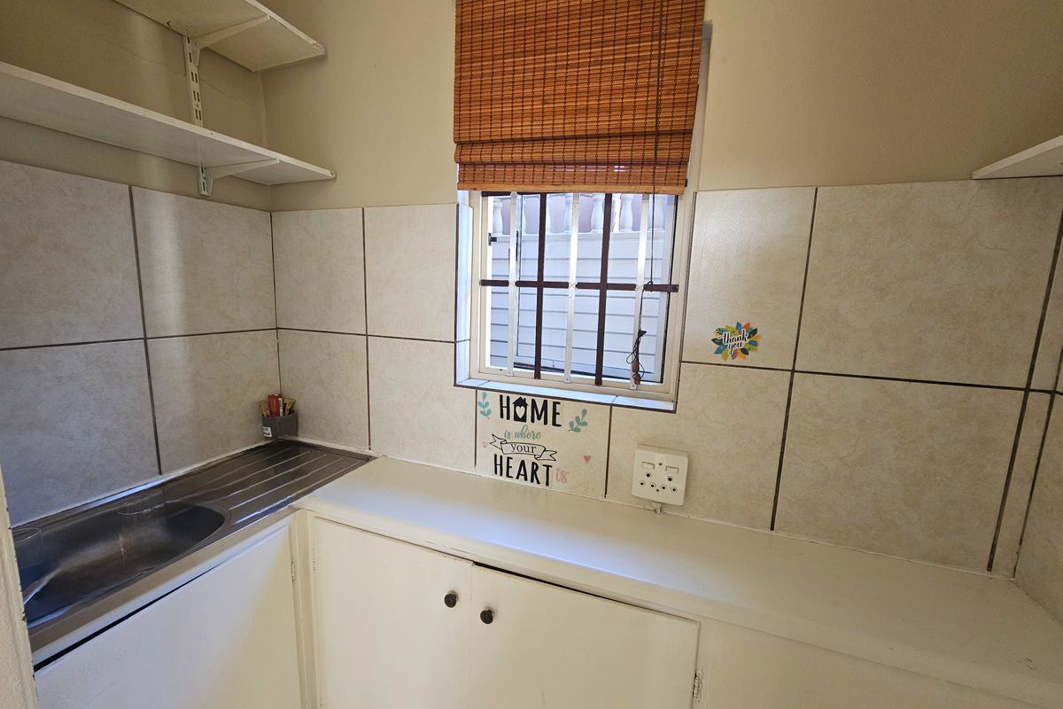 A functional scullery or utility area featuring built-in cabinetry, a stainless steel sink, tiled splashbacks, and wall-mounted shelving.