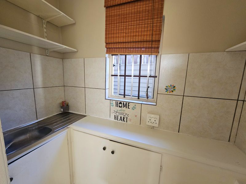 A functional scullery or utility area featuring built-in cabinetry, a stainless steel sink, tiled splashbacks, and wall-mounted shelving.