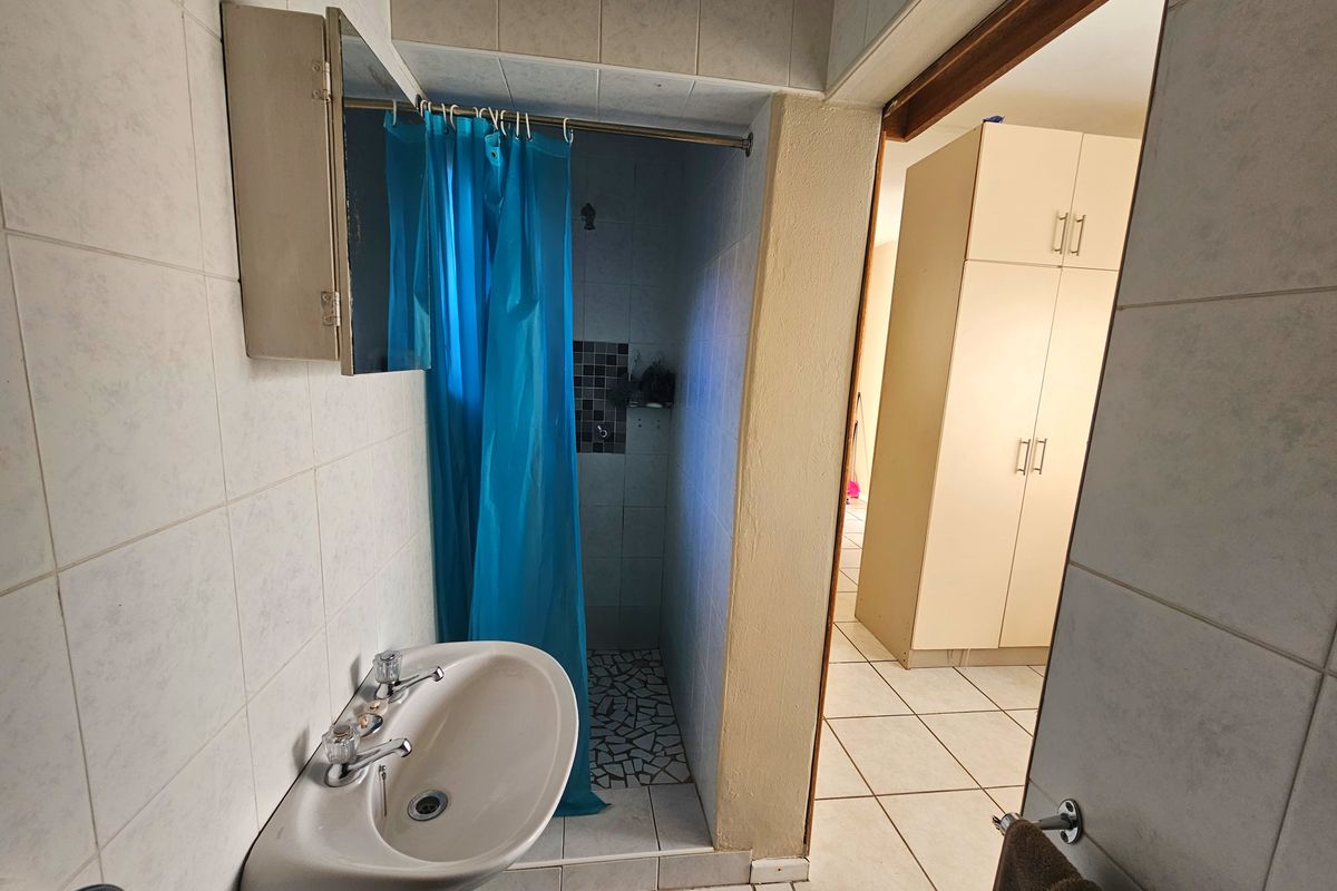 A functional bathroom featuring a wall-mounted basin and a tiled shower area, with adjacent built-in storage cabinetry visible in the hallway.