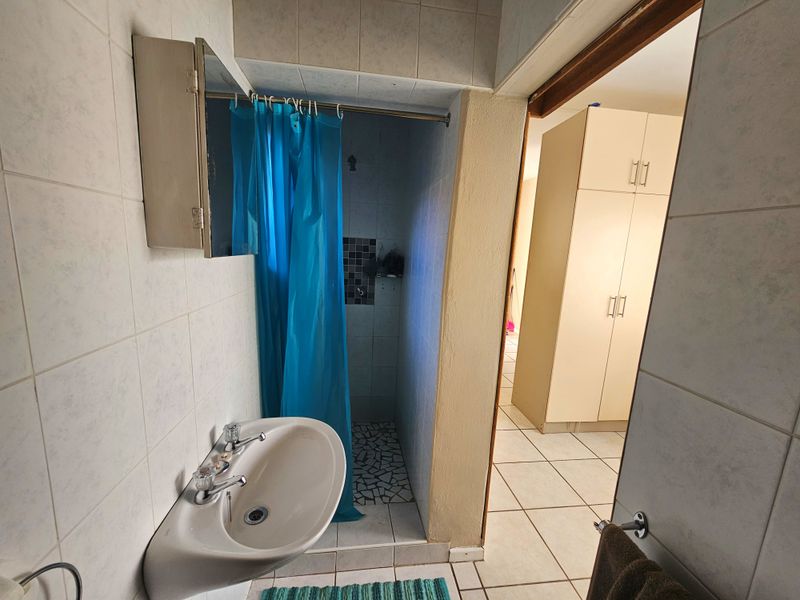 A functional bathroom featuring a wall-mounted basin and a tiled shower area, with adjacent built-in storage cabinetry visible in the hallway.