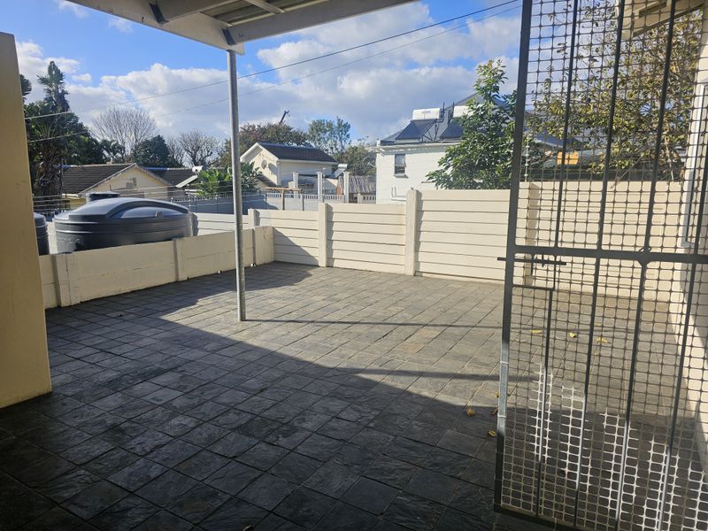 A paved outdoor patio area featuring a covered roof, security gate, and perimeter walling, providing a functional space for outdoor living.