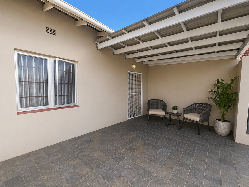 A clean, covered outdoor patio area featuring tiled flooring, a secure entrance gate, and protective security bars on the window.