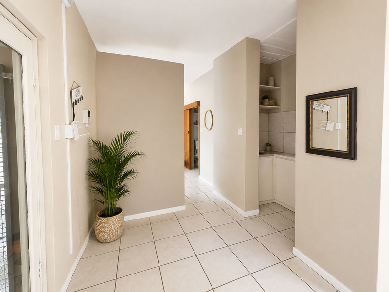 A bright and neutral hallway featuring tiled flooring, built-in shelving, and a sliding door, providing a clean and functional transition space.