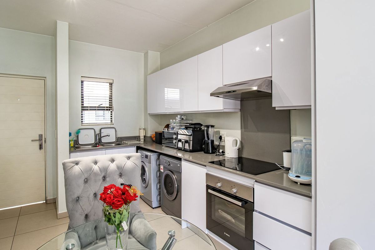 Modern kitchen featuring white high-gloss cabinetry, stone countertops, integrated oven and hob, and dedicated space for laundry appliances.