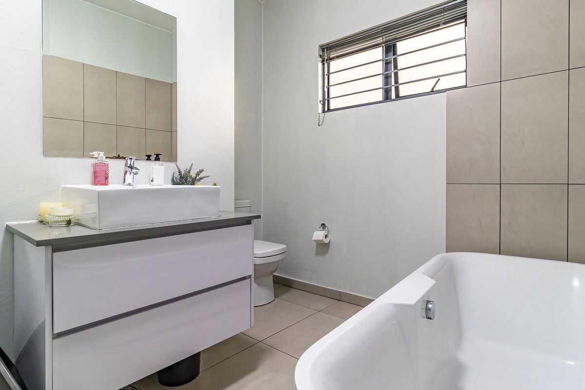 Modern bathroom featuring a white vanity with vessel sink, a bathtub, and neutral wall tiling with a window providing natural light.