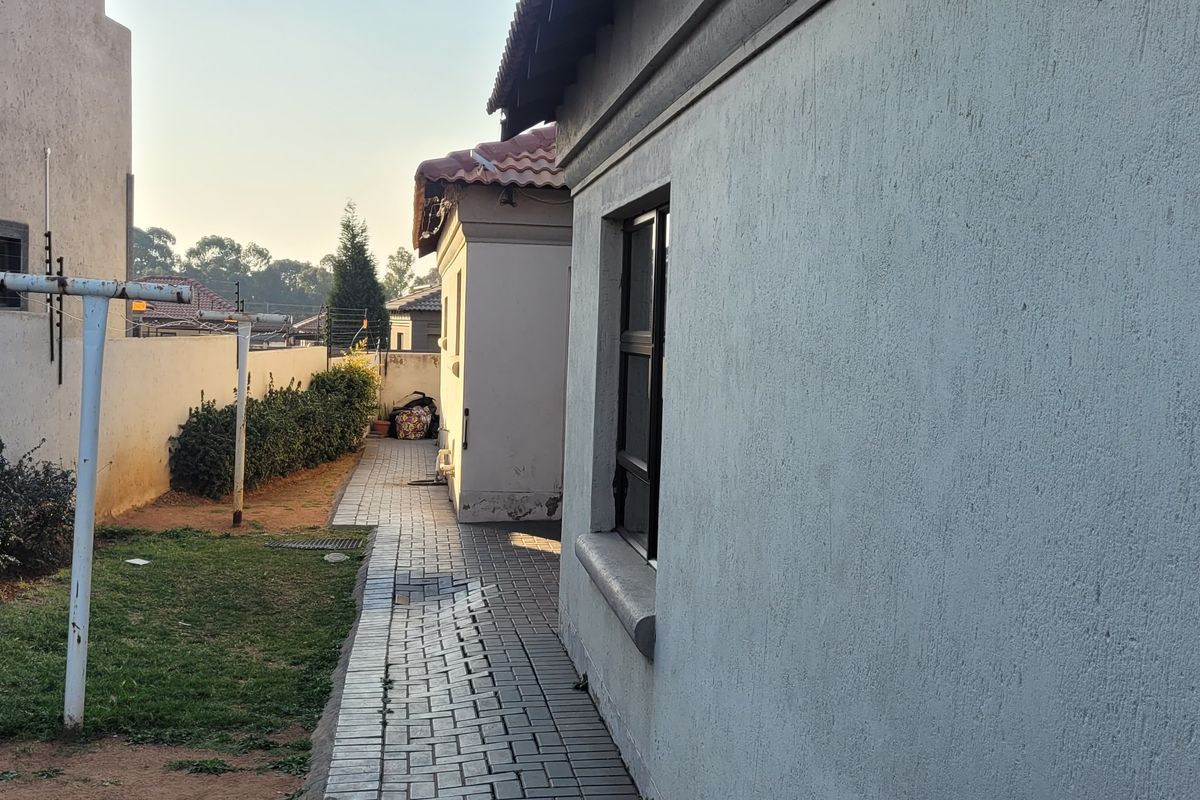 A side view of the property showing a paved walkway, boundary wall, and exterior building facade with a tiled roof.