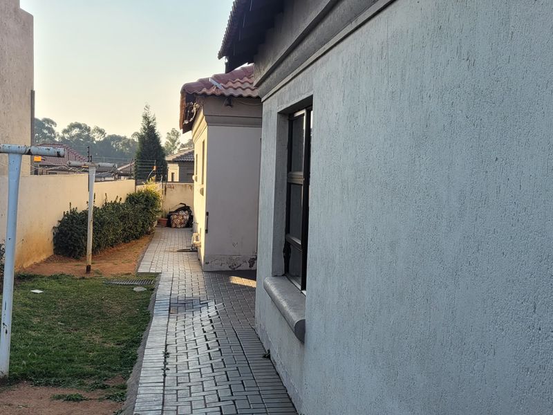 A side view of the property showing a paved walkway, boundary wall, and exterior building facade with a tiled roof.