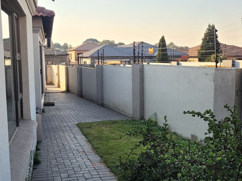 A side exterior view showing a paved walkway, perimeter wall with electric fencing, and access to the home via a sliding glass door.