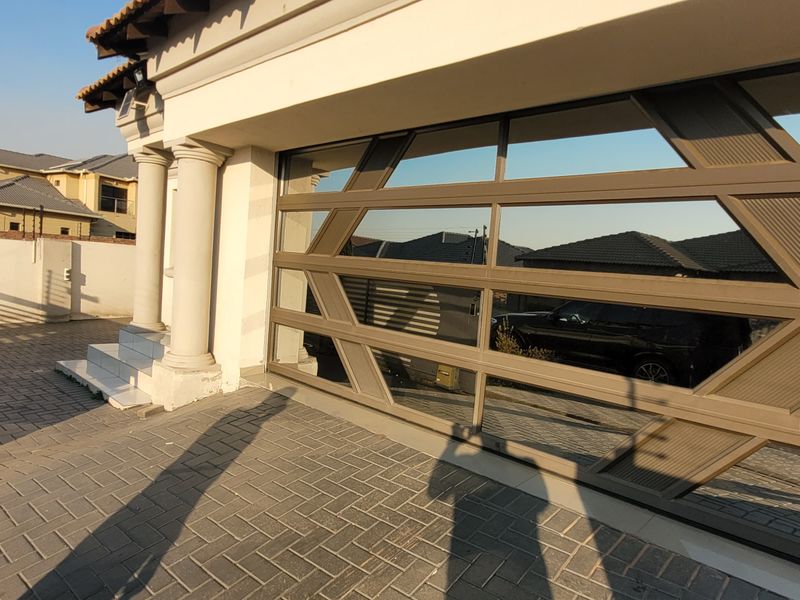 Front exterior view of the property featuring a paved driveway, modern decorative electric gate, and structural concrete columns.