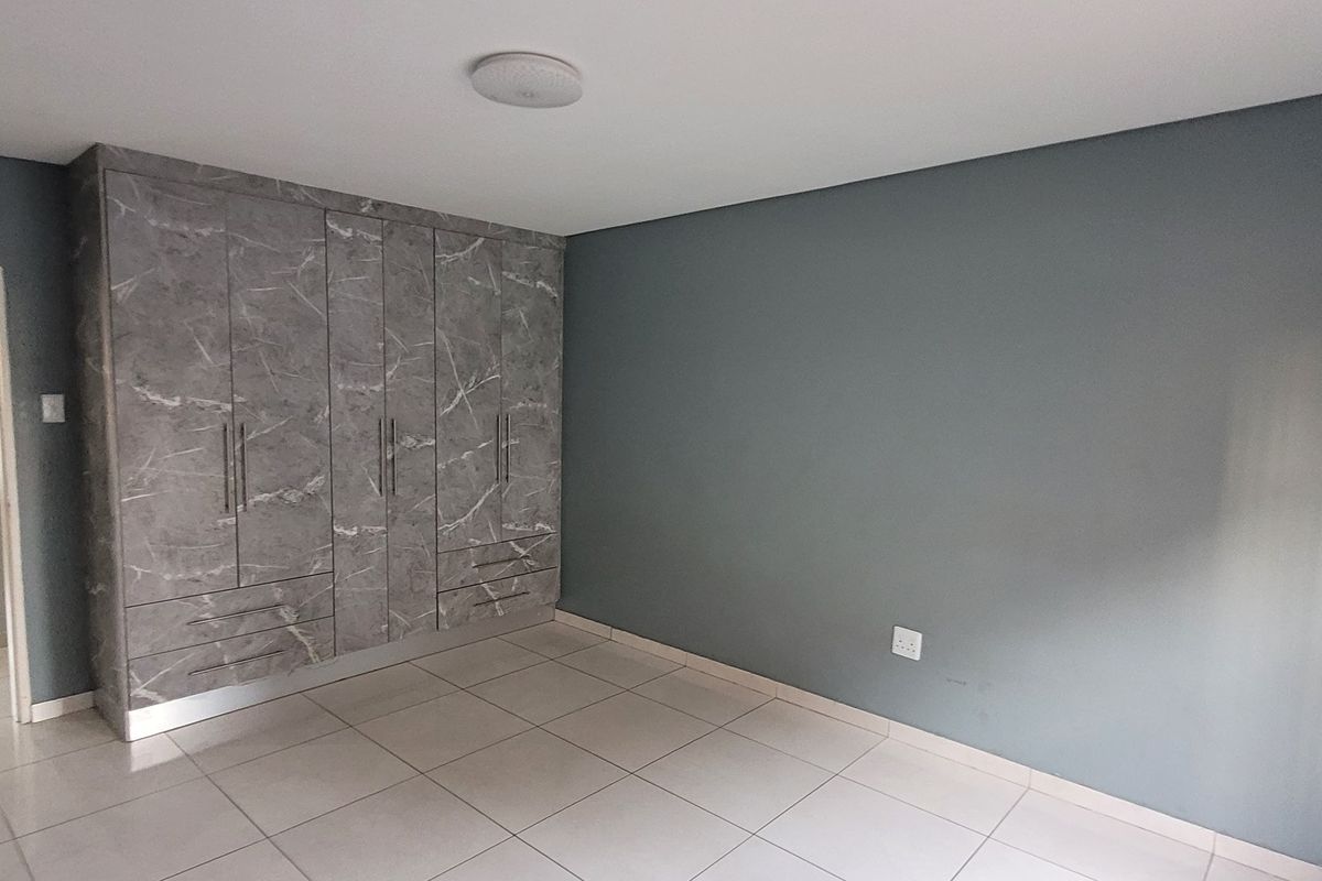 A clean, empty bedroom featuring modern grey marble-finish built-in cupboards and neutral tiled flooring, offering a versatile space ready for personalization.
