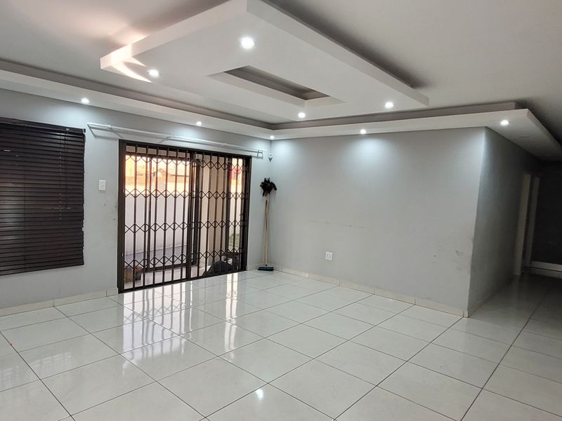 Spacious, empty living area featuring modern recessed ceiling lighting, large format floor tiles, and a sliding door with security gate access to the exterior.