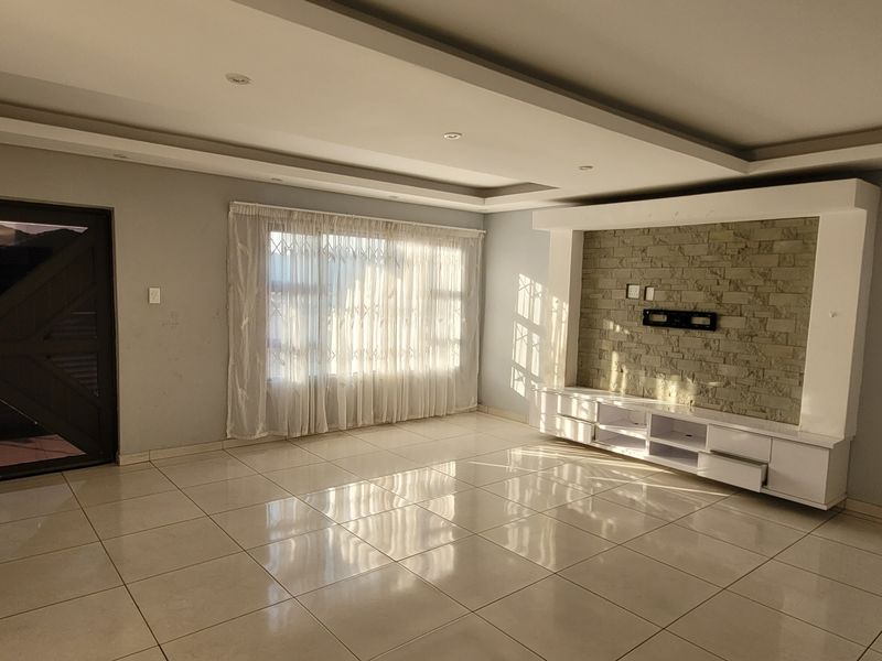 Spacious living room featuring a modern recessed ceiling, stone feature wall with built-in media console, tiled flooring, and a wall-mounted air conditioning unit.