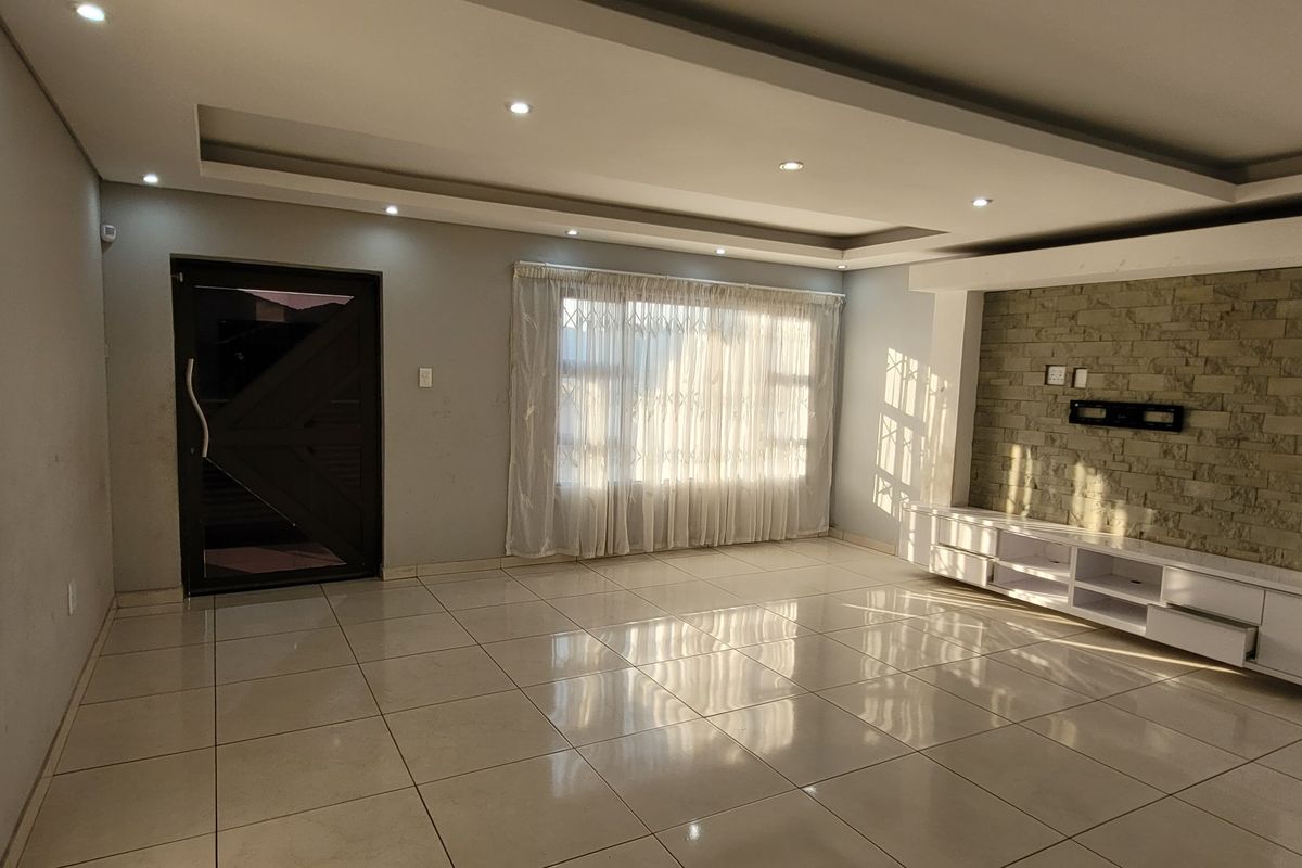 Spacious living room featuring tiled floors, a tray ceiling with recessed lighting, and a built-in media console set against a stone feature wall.