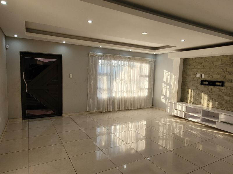 Spacious living room featuring tiled floors, a tray ceiling with recessed lighting, and a built-in media console set against a stone feature wall.