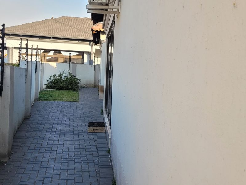 A side passage featuring paved flooring, boundary walls with electric fencing, and an exterior air conditioning unit.