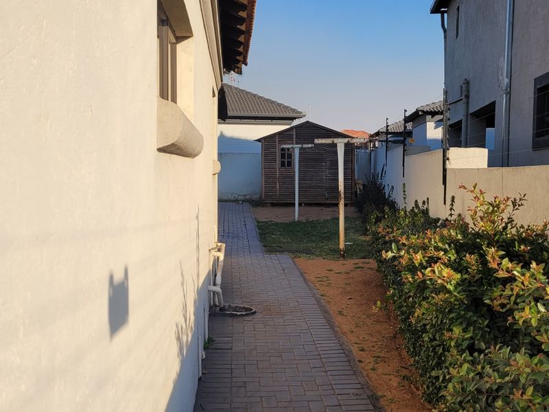A side exterior view showing a paved walkway, boundary wall with electric fencing, and a small garden shed at the rear of the property.