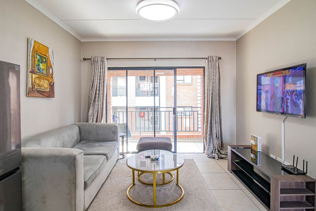 A well-maintained living room featuring tiled flooring and a large sliding glass door providing access to an outdoor balcony area.