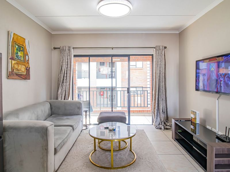 A well-maintained living room featuring tiled flooring and a large sliding glass door providing access to an outdoor balcony area.