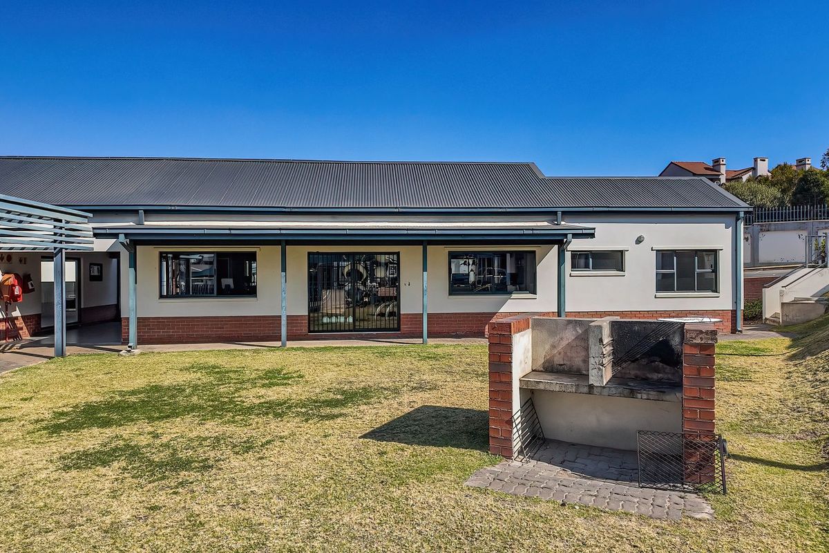 Rear exterior view of the apartment featuring a covered patio, a built-in brick braai area, and a private lawn space.