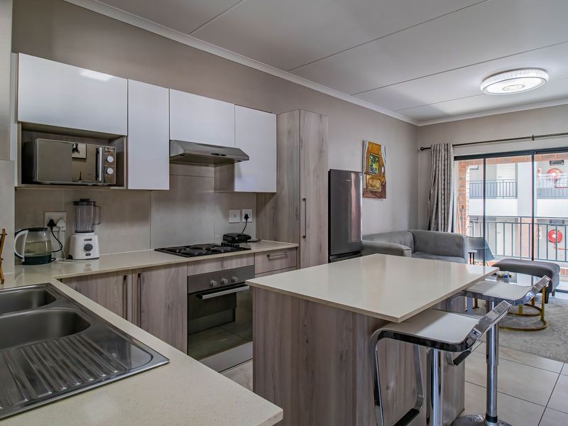 Modern open-plan kitchen featuring light wood cabinetry, stone countertops, built-in appliances, and a central island, flowing into a living area with balcony access.