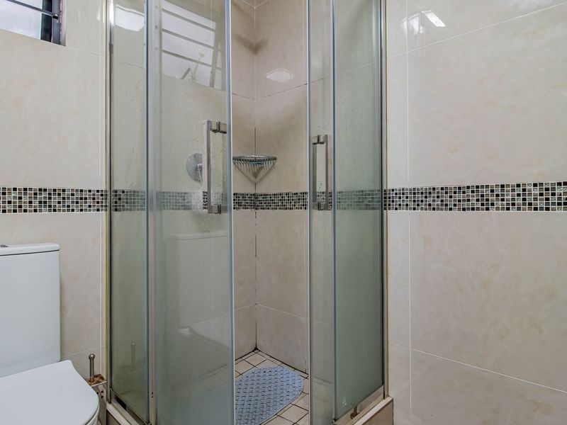 A functional bathroom featuring a glass-enclosed shower, a standard toilet, and neutral wall tiling with a decorative mosaic accent border.