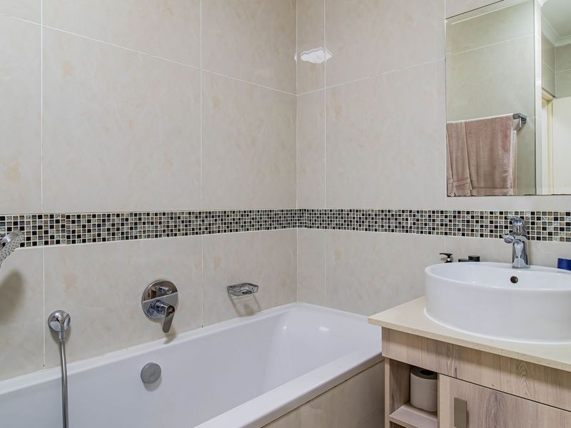 A well-maintained bathroom featuring a bathtub with a handheld shower, a modern countertop basin, vanity storage, and decorative mosaic tile accents.