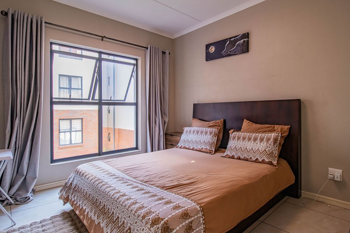 A well-maintained bedroom featuring tiled flooring, neutral wall tones, and a large aluminium-framed window providing natural light.