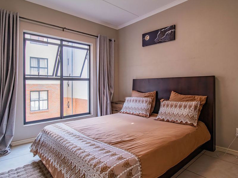 A well-maintained bedroom featuring tiled flooring, neutral wall tones, and a large aluminium-framed window providing natural light.