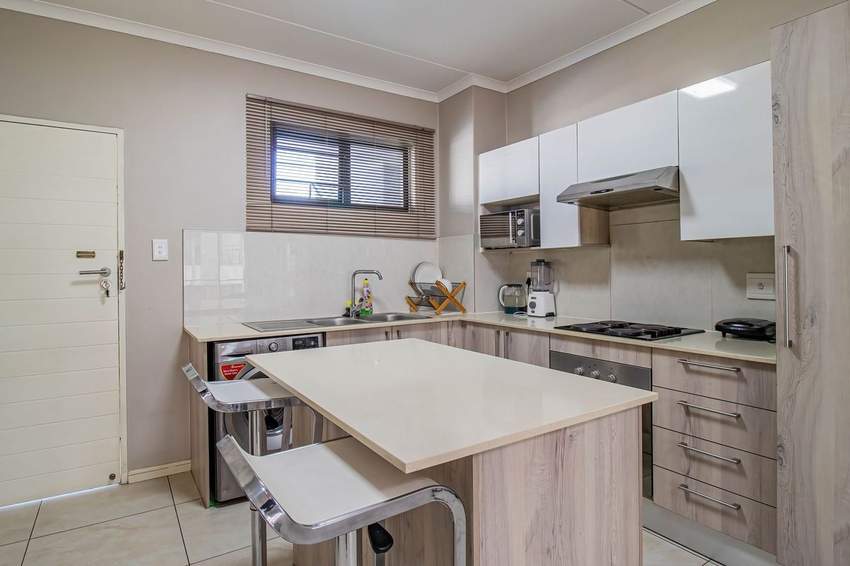 Modern kitchen featuring light wood-grain cabinetry, stone countertops, integrated appliances, and a central breakfast island with tiled flooring.