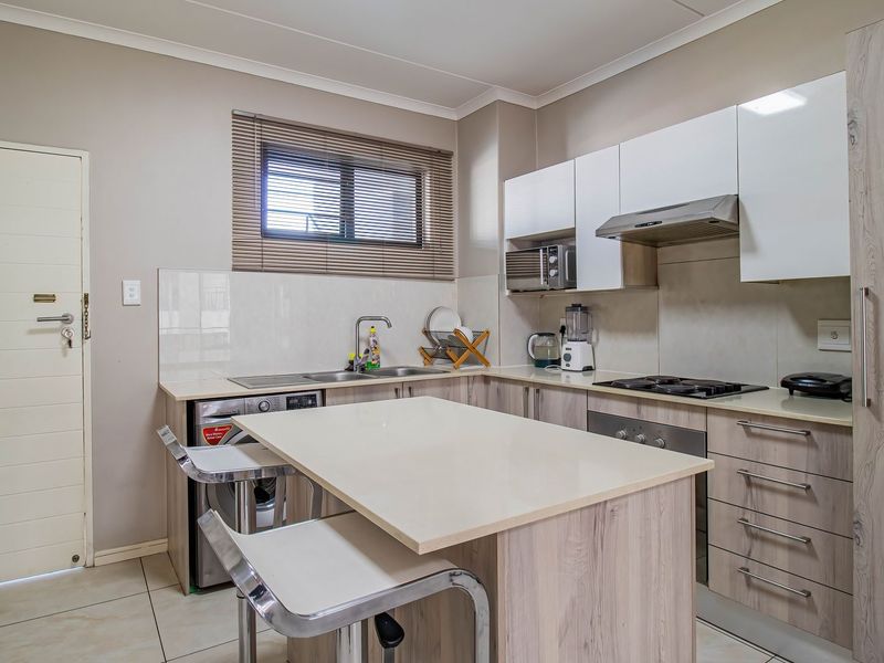 Modern kitchen featuring light wood-grain cabinetry, stone countertops, integrated appliances, and a central breakfast island with tiled flooring.